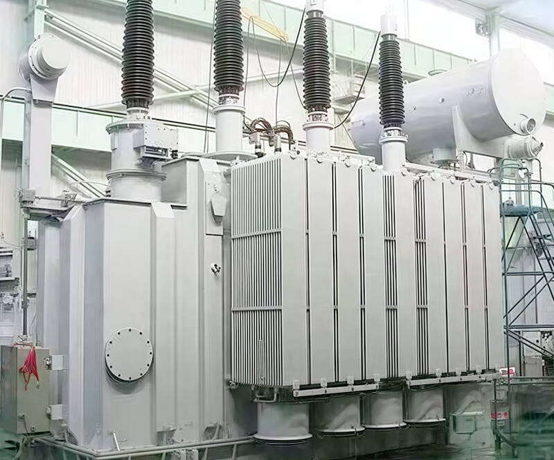 Side view of a oil immersed electrical transformer stationed inside the manufacturer's facility, emphasizing its size and quality control.